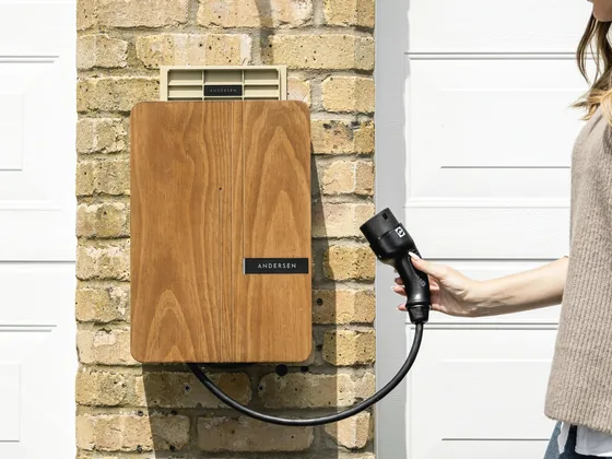 Wandladestation aus Holz an einer Klinkerwand, das Ladekabel wird in der Hand gehalten.