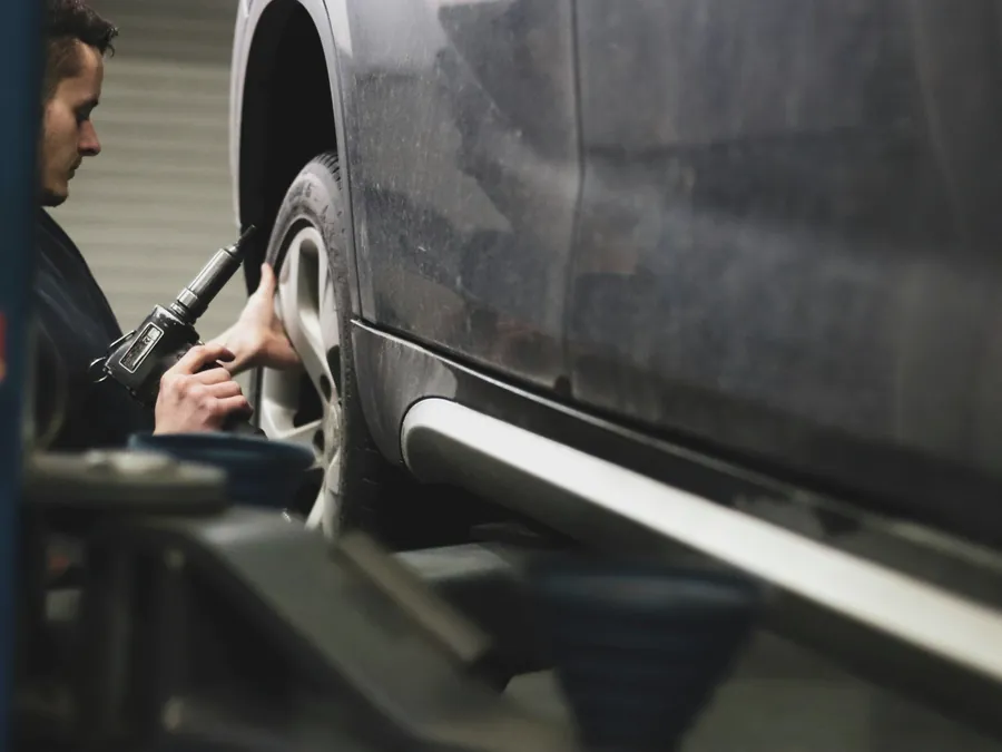 Mechaniker arbeitet mit Werkzeug an der Seite eines angehobenen Fahrzeugs.