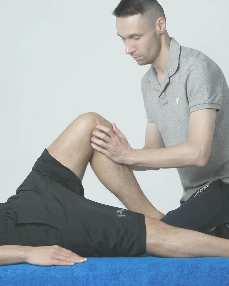 Therapeut behandelt konzentriert das Knie einer auf der Liege liegenden Person.