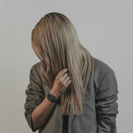 Blondes Langhaar fällt nach vorn über das Gesicht, heller Hintergrund.